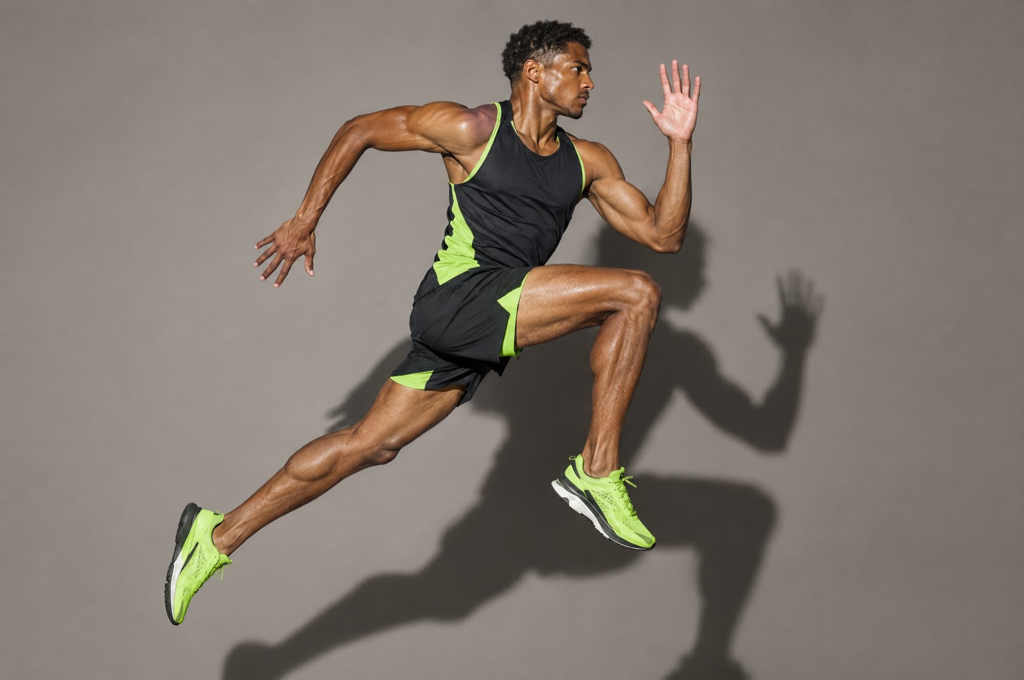 An athlete mid-jump in black and lime running kit on a grey studio backdrop