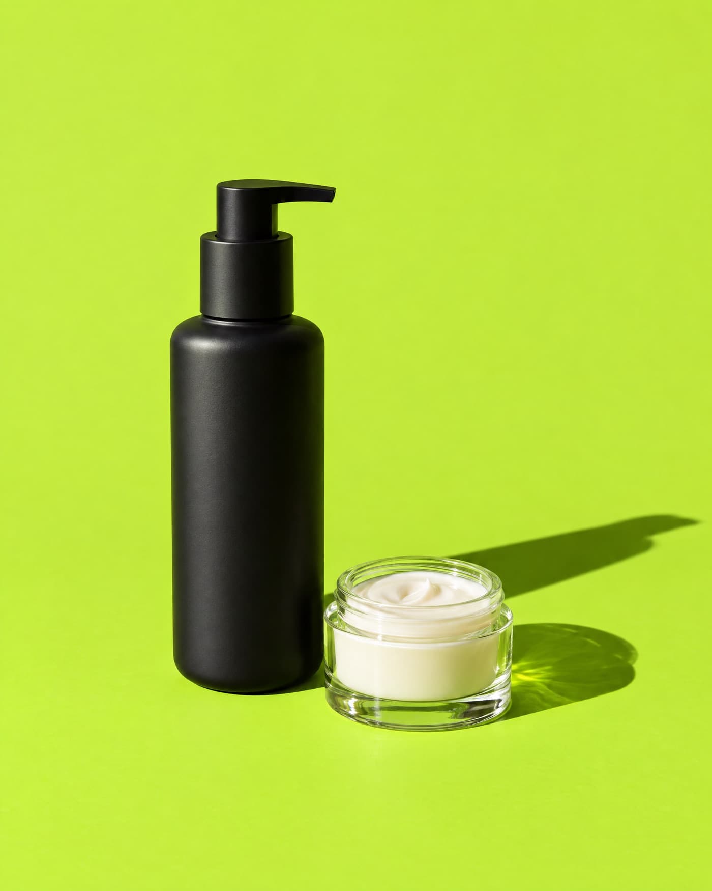 A matte black skincare bottle and a glass jar on an acid green backdrop